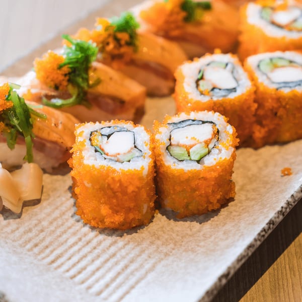 A plate of Kiku Sushi's California rolls and salmon nigiri, garnished with roe and green onions.