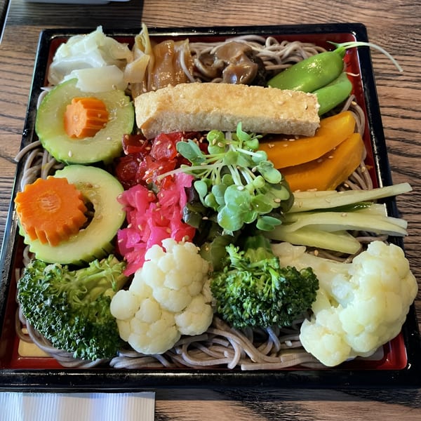 A colorful Kiku Sushi & Vegetarian bento box with soba noodles, various vegetables, and tofu.