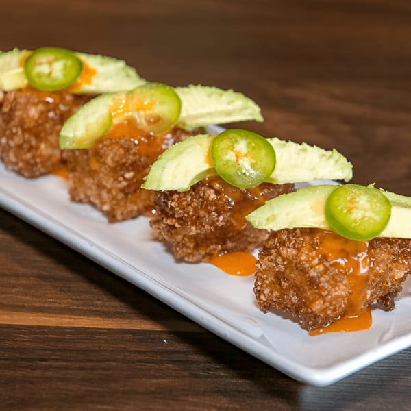 Four crispy rice squares topped with avocado slices, jalapeños, and orange sauce on a white plate.