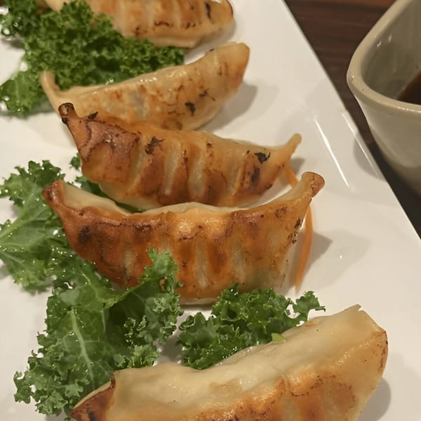 Five golden-brown Kiku Sushi gyoza dumplings with kale garnish and a side of dipping sauce.