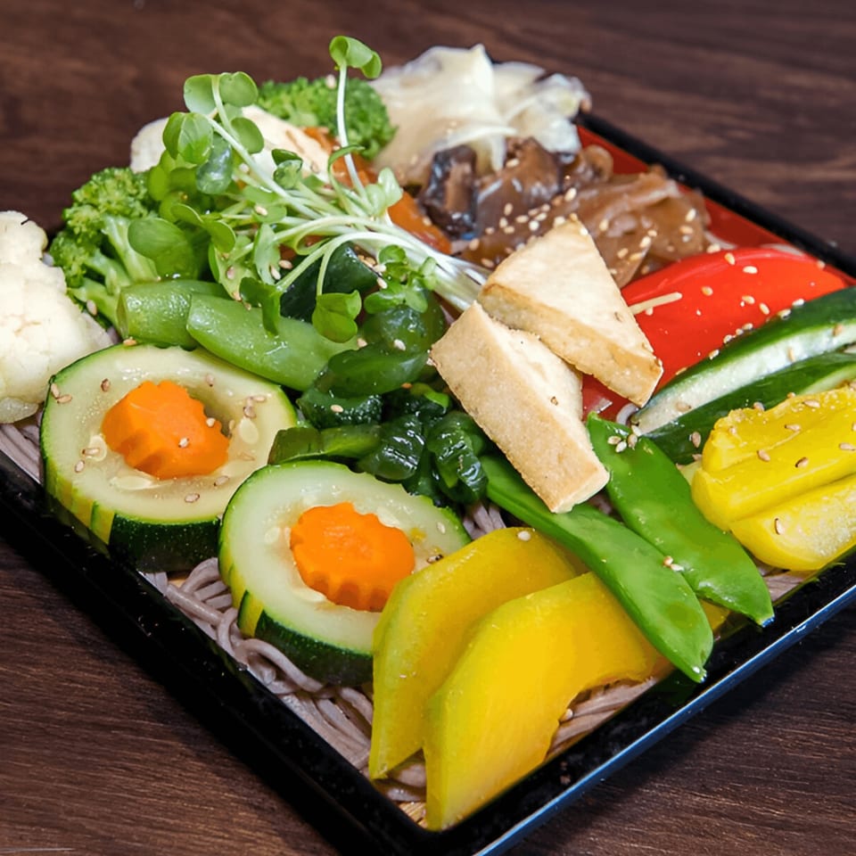 A vibrant Kiku Sushi & Vegetarian bento box filled with fresh vegetables, tofu, and soba noodles.
