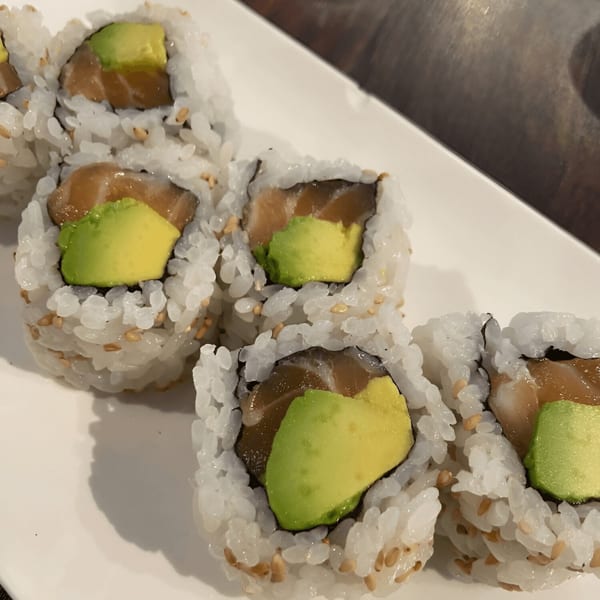 Close-up of Kiku Sushi's salmon and avocado sushi rolls with sesame seeds on a white plate.