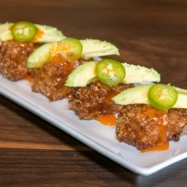 Four crispy rice cakes topped with avocado slices, jalapeños, and orange sauce on a white plate.