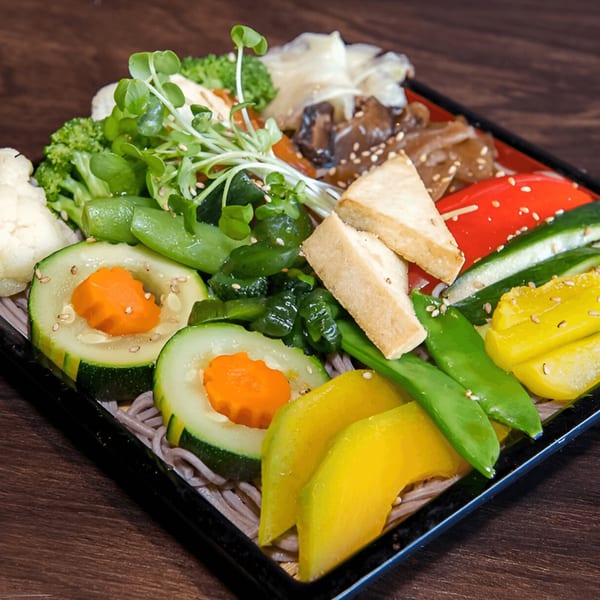 A vibrant Kiku Sushi & Vegetarian bento box filled with fresh vegetables, tofu, and soba noodles.