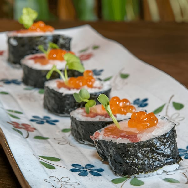 Five pieces of Kiku Sushi's maki rolls with salmon, roe, and microgreens on a floral plate.